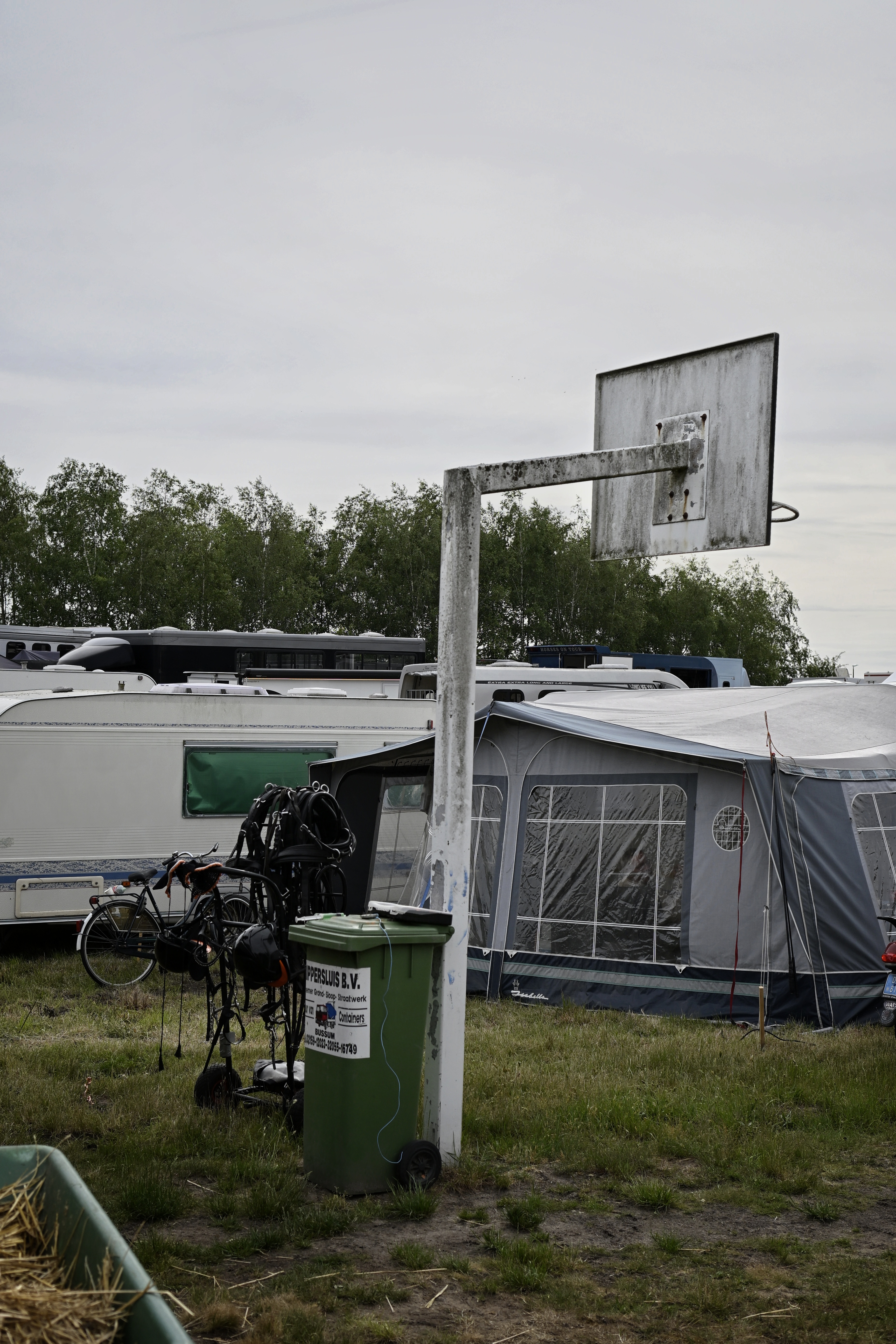 A hoop on a pole with a bin next to it and a tent and trailer behind it.