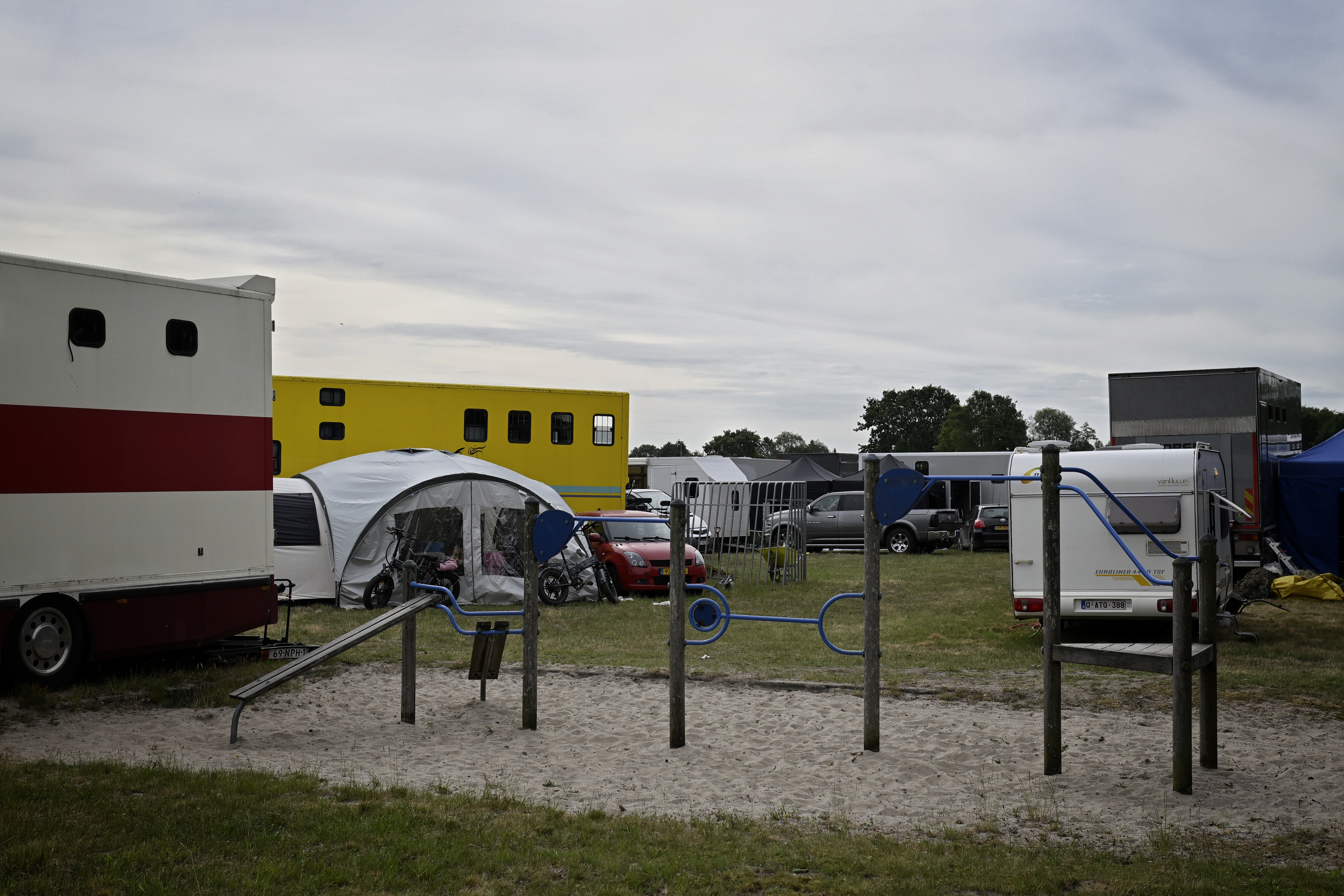 Playground equipment standing in white sand and surrounded by tents, trailers and what not.