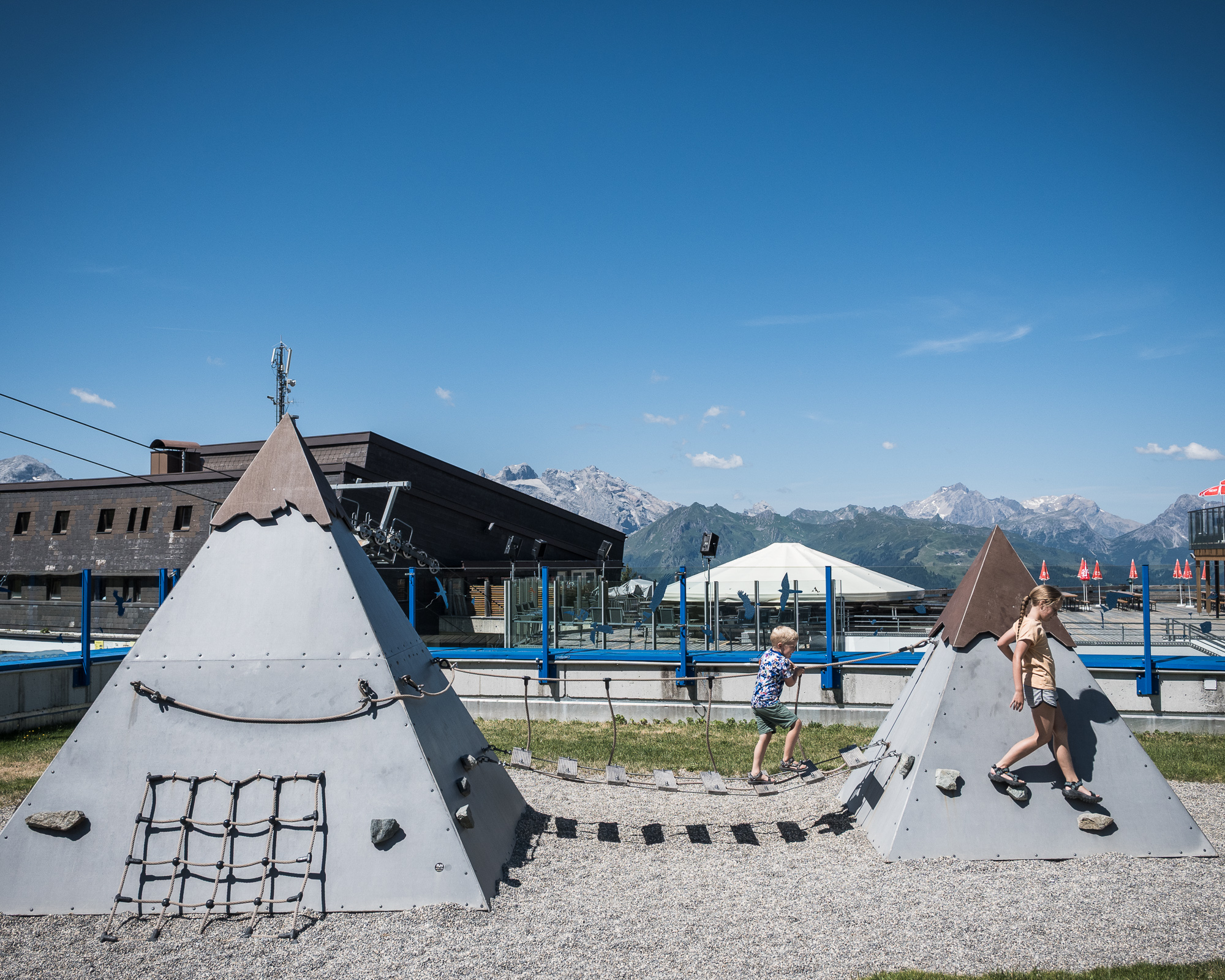 A young boy and girl climbing in a playground where the features are shaped like mountains, with mountains in the background.