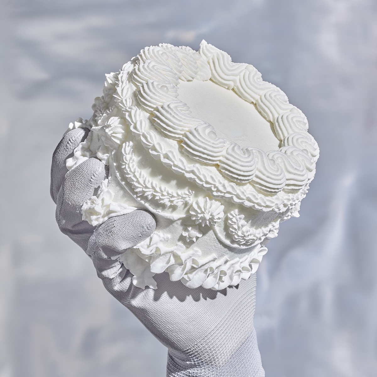 Cover of the album IJSLAND 2. A small white cake held a white-gloved hand.