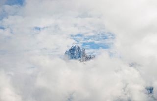 A field of clouds with an opening in the center, showing a single mountain peak.