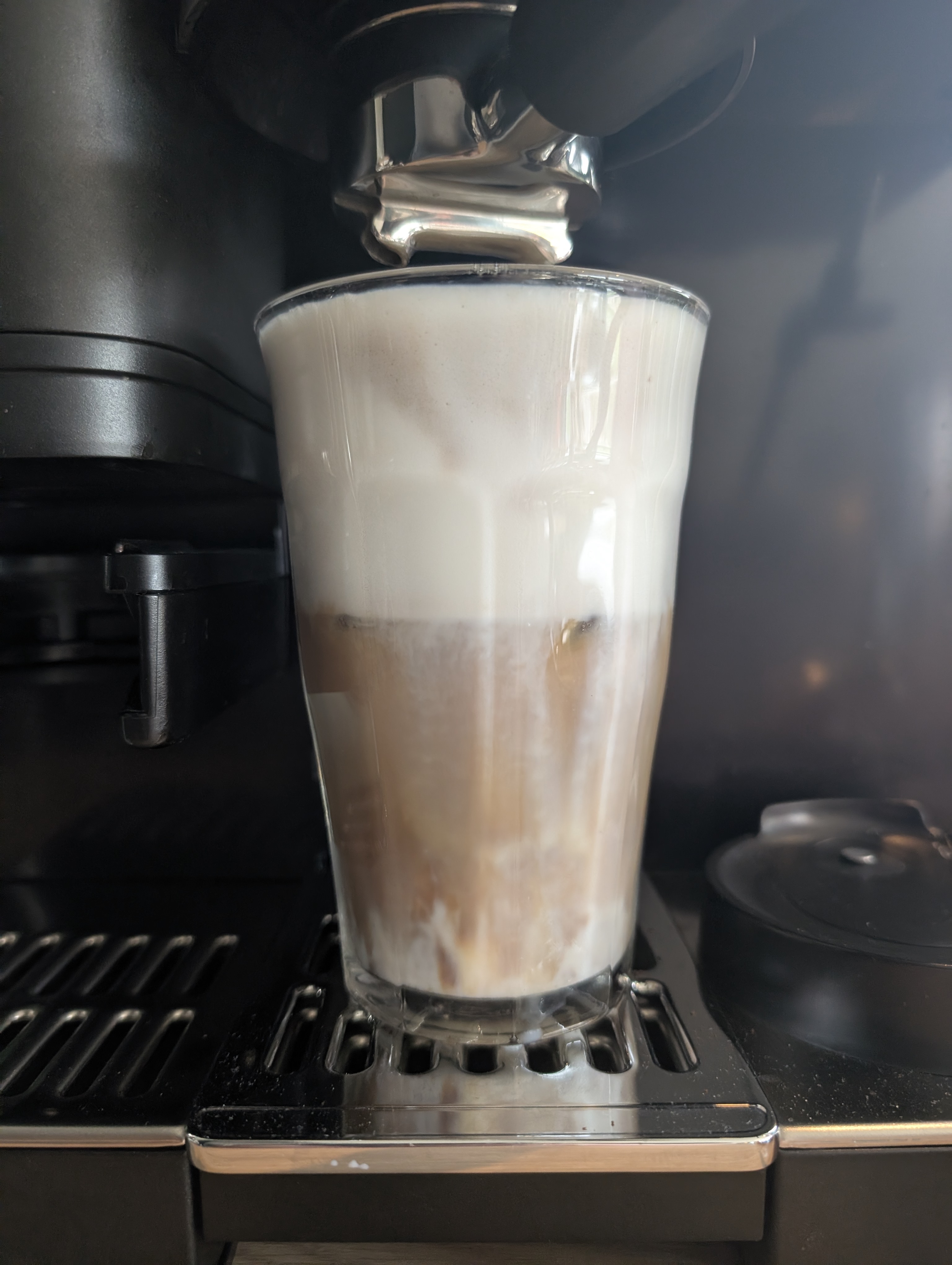 A glass of fancy coffee with foamy milk sitting in a coffee maker/machine.